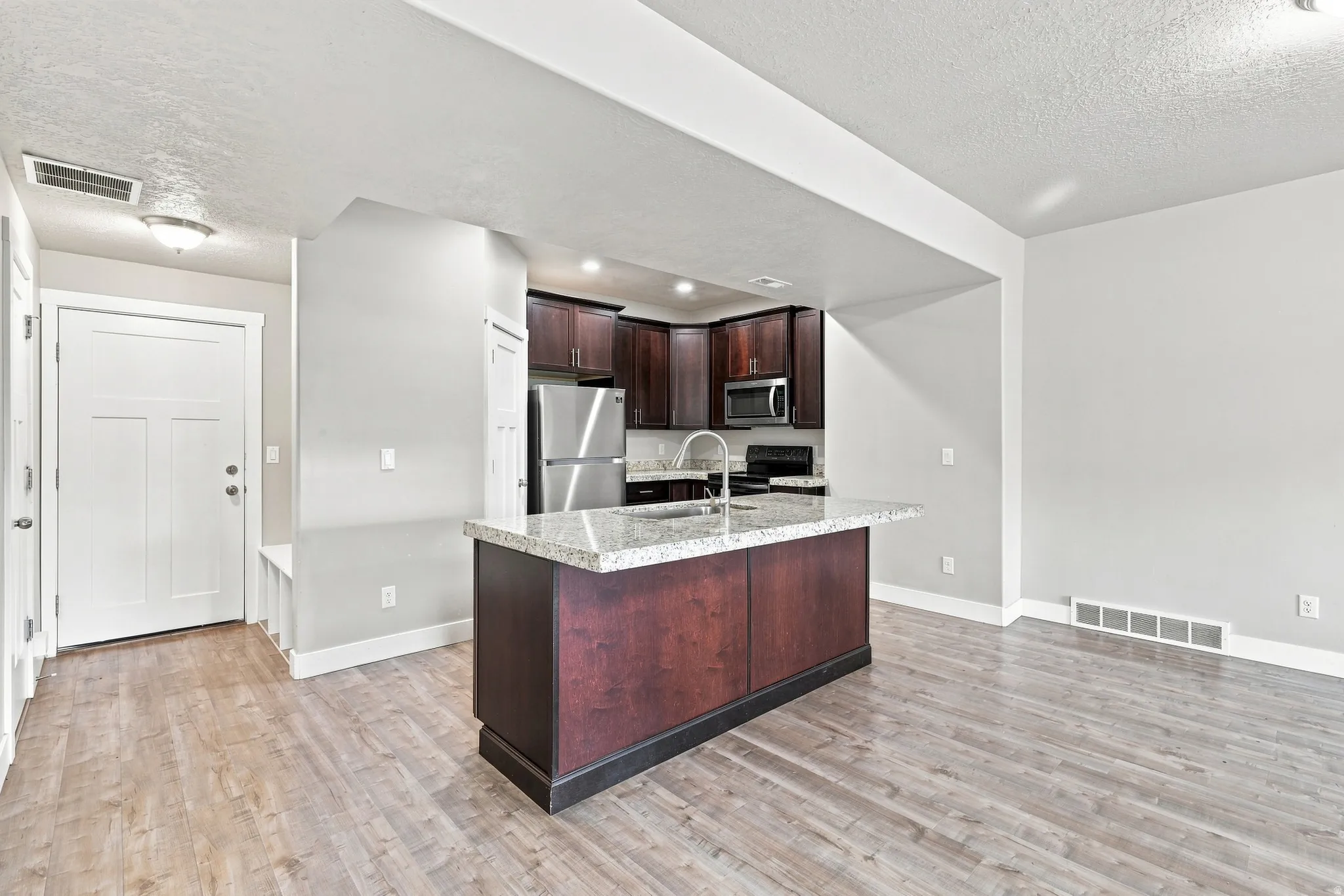 Kitchen island with a granite-style countertop, wood-finish flooring, and dark wood cabinetry