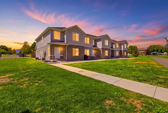 Two-story residential building with siding and stone veneer, multiple windows, and a concrete walkway