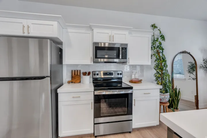 Stainless steel refrigerator, white shaker-style cabinetry, stainless steel microwave, electric range, and white subway tile backsplash