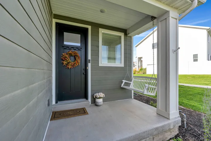 Covered front porch with concrete flooring, plank siding exterior, and a white porch swing