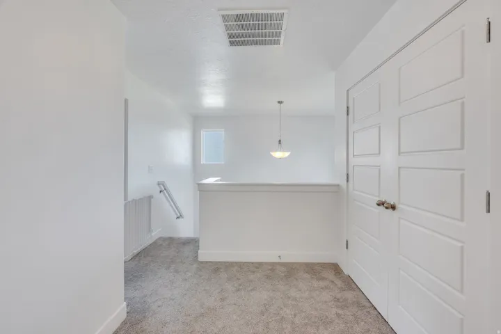 Light grey carpeting, white interior doors with contemporary paneling, white walls, and a recessed ceiling vent