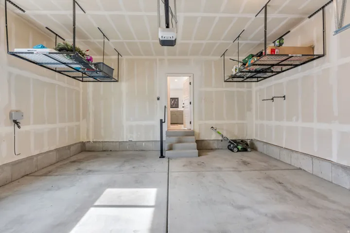 Concrete flooring, two ceiling-mounted storage racks, automatic garage door opener, interior access door, and a built-in step with a handrail