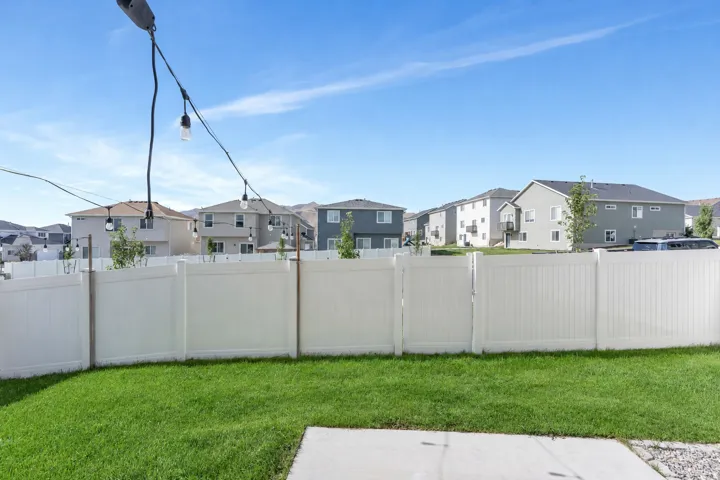 Expansive grassy lawn with a white privacy fence and concrete patio