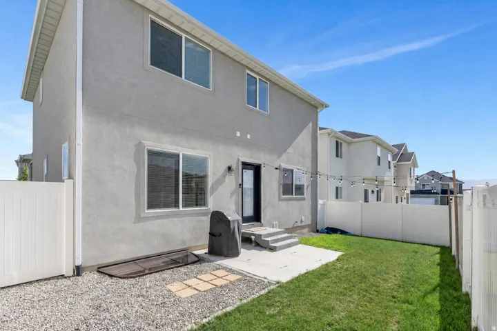 Stucco exterior featuring multiple windows, a concrete patio, and a grass lawn, enclosed by a white privacy fence