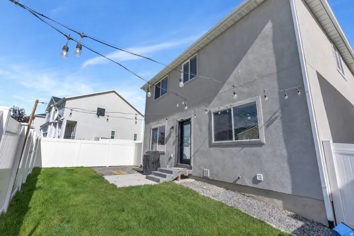 Stucco exterior with multiple windows, a rear entry door, a concrete patio, and a fenced yard with grass and gravel