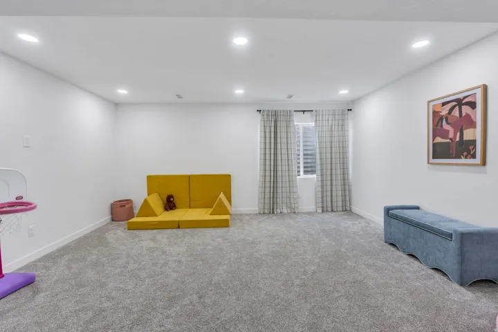 Spacious room featuring neutral carpet, white walls, recessed lighting, and a window with blinds and curtains