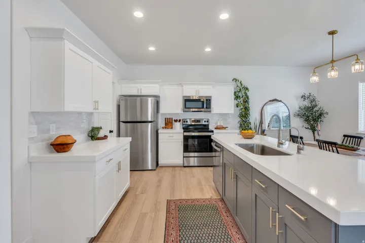 White shaker cabinetry with crown molding, stainless steel appliances, light wood-finish flooring, a kitchen island with a built-in sink, and recessed lighting