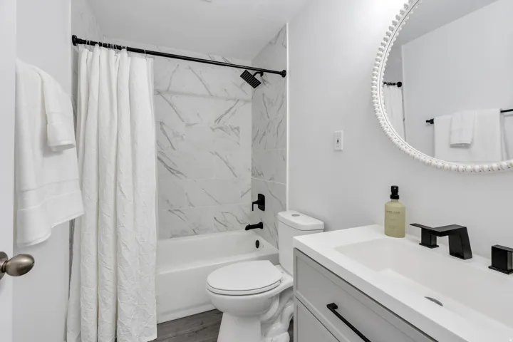 White subway tile shower surround, black matte fixtures, single vanity with integrated sink, and wood-finish flooring