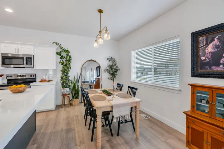White cabinetry, stainless steel appliances, light wood-finish flooring, recessed lighting, and a linear pendant light fixture