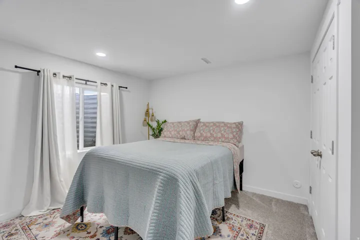 Bright secondary bedroom featuring recessed ceiling lighting, large windows with sheer curtains, upholstered headboard, wood-finish flooring, and geometric patterned area rug