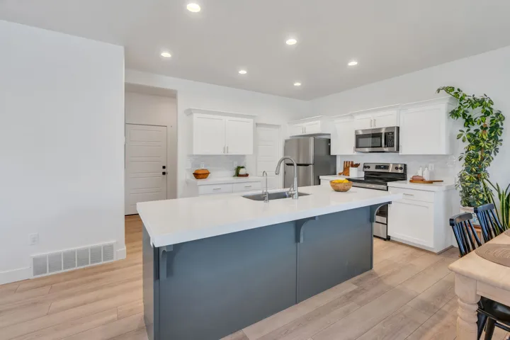 Kitchen featuring a central island with an undermount sink, white cabinetry, stainless steel appliances, and wood-finish flooring