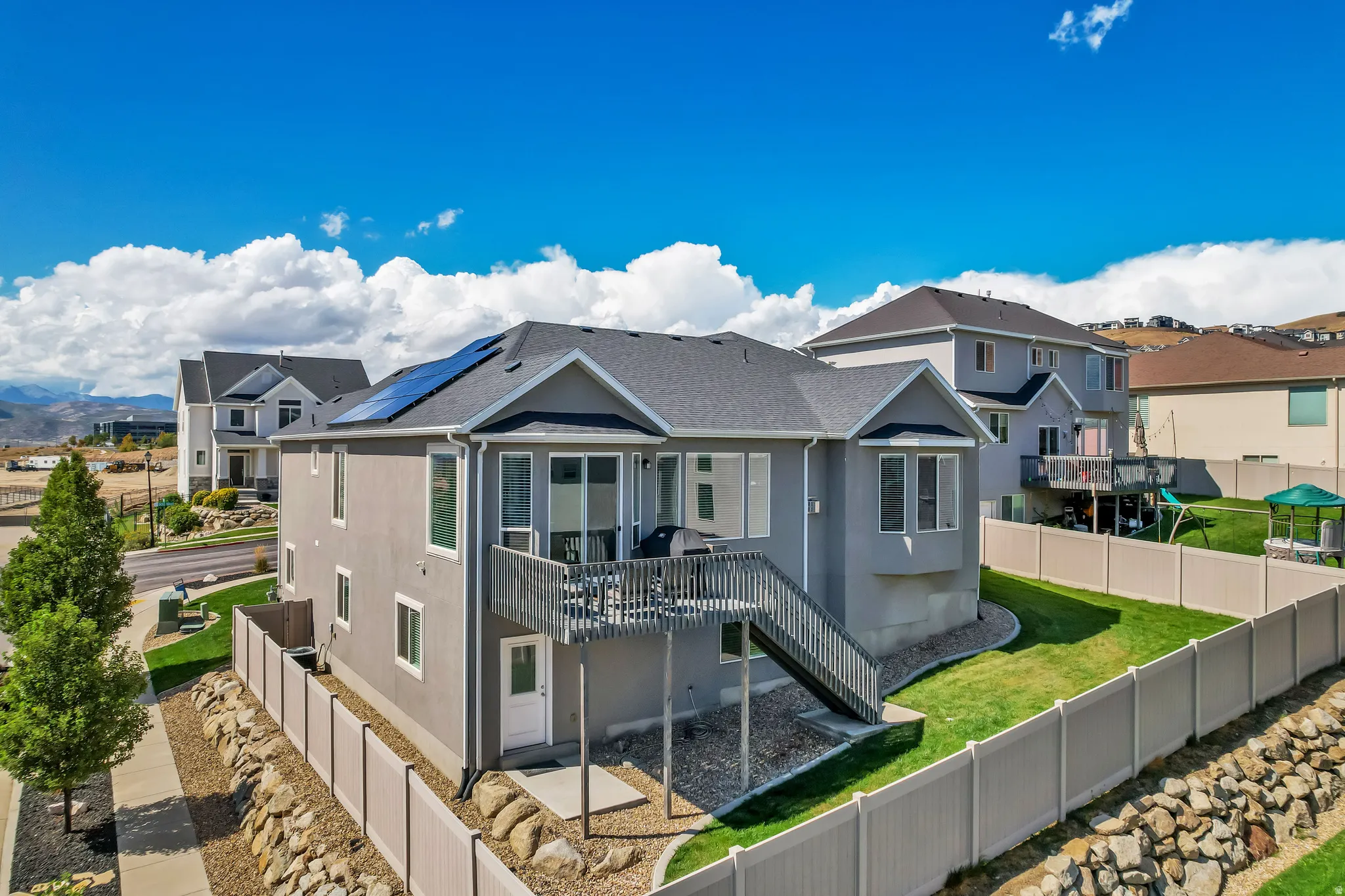 Two-story residence featuring a private deck with exterior stairs, solar panels on the roof, and a fenced backyard with a sloped lawn