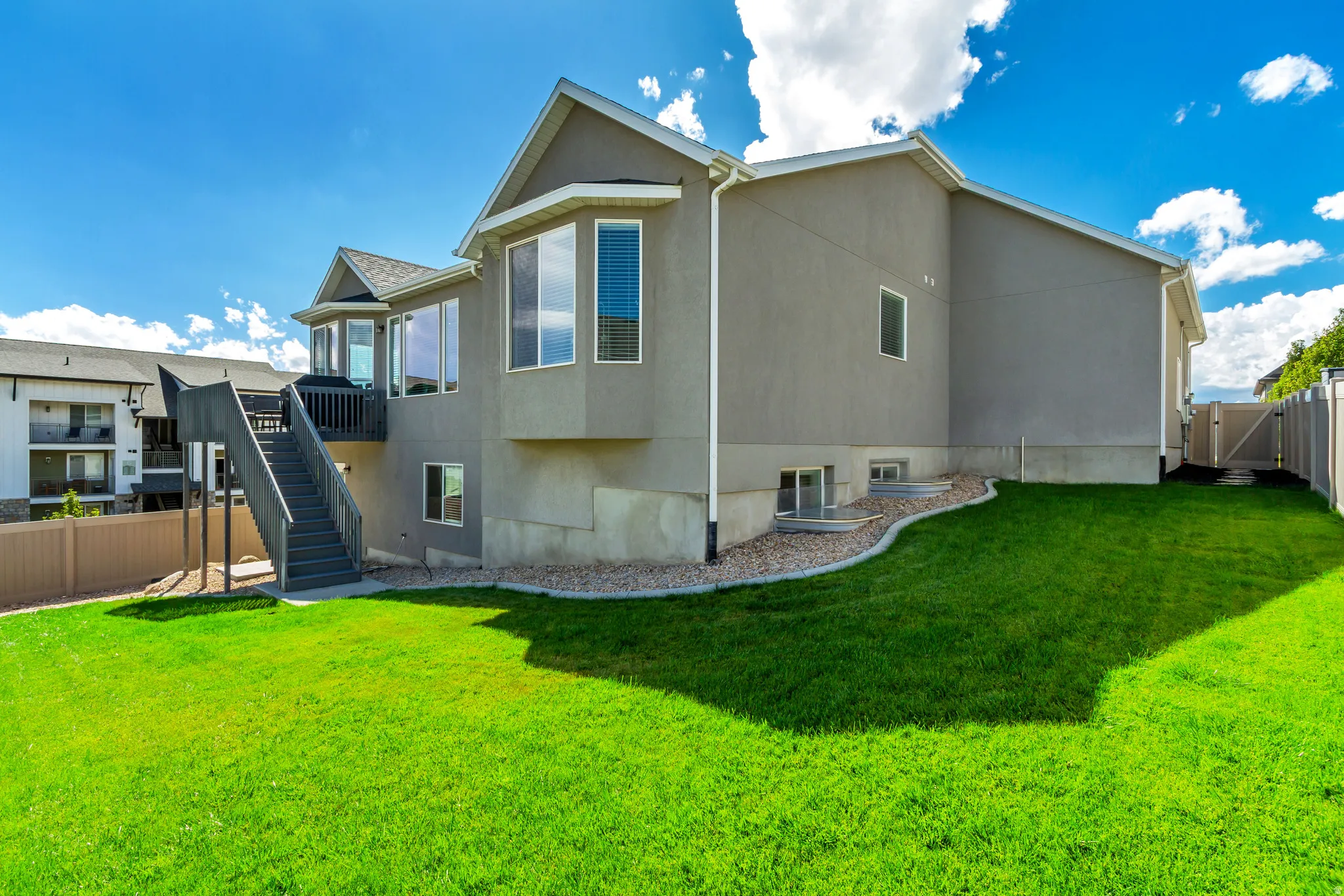Spacious backyard featuring a manicured lawn, a multi-level deck with stairs, a privacy fence, and a gate