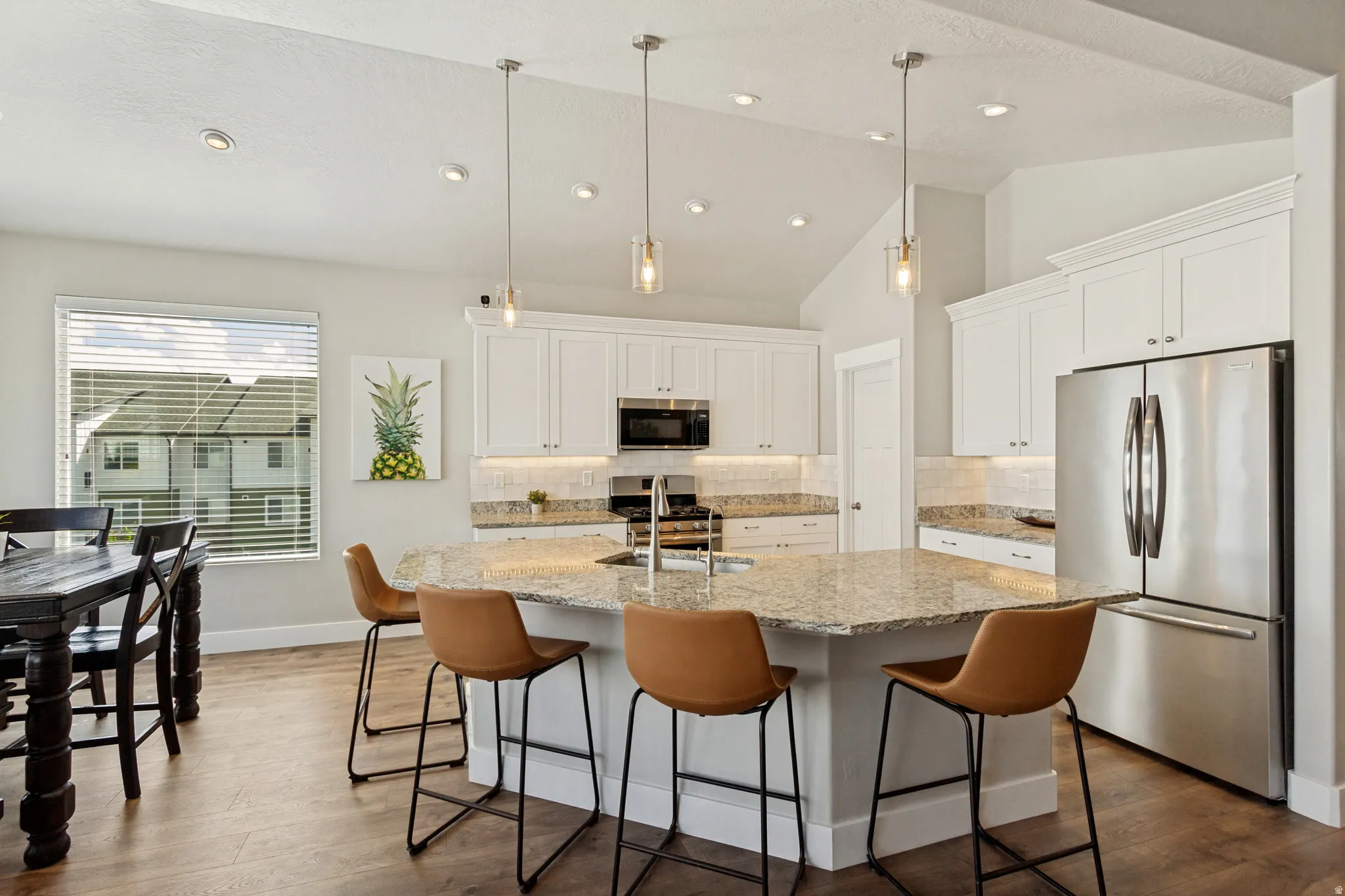Kitchen featuring a large island with stone countertop, pendant lighting, stainless steel appliances, and white cabinetry