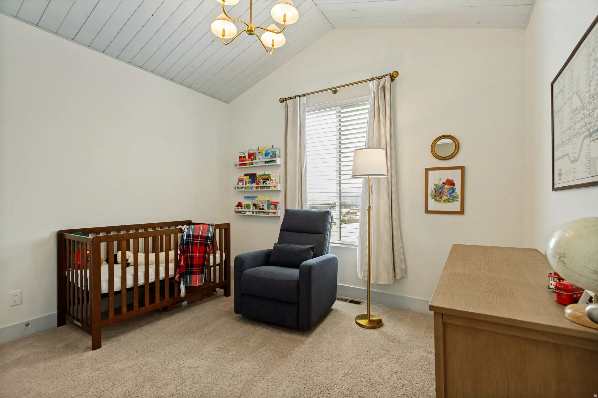 Bright nursery featuring vaulted shiplap ceiling with integrated lighting, wood-finish crib, plush carpeting, and glass door with shutters opening to natural light