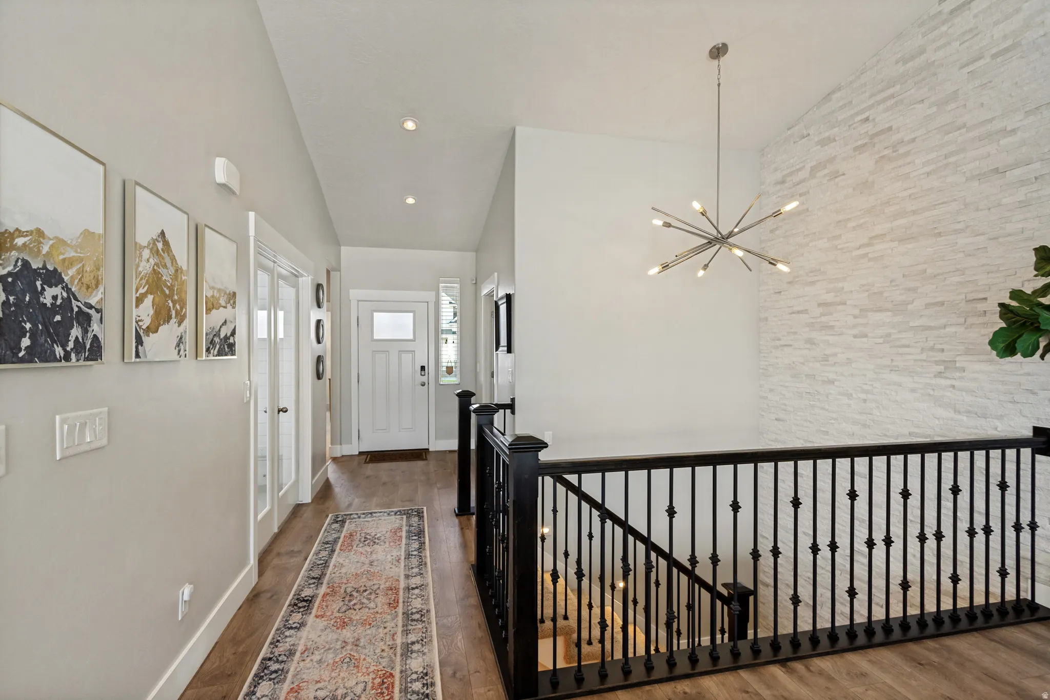 Vaulted ceiling with an exposed white brick accent wall, modern sputnik chandelier, wood-finish flooring, and a white paneled entry door with frosted glass insert