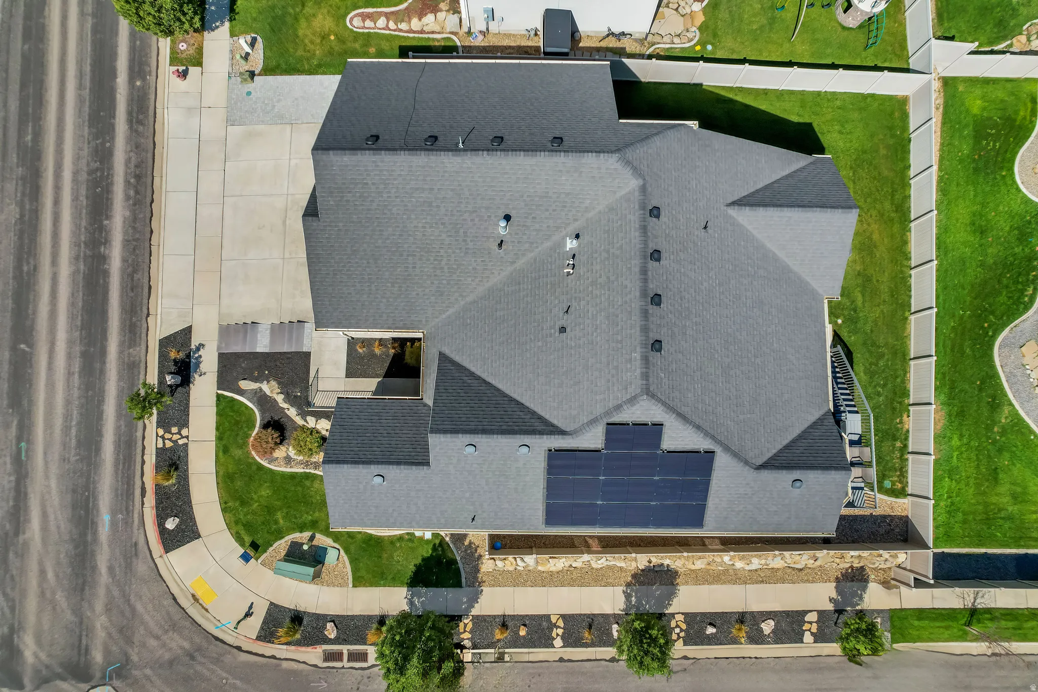 Asphalt shingle roof with solar panel array, concrete driveway, and manicured lawn