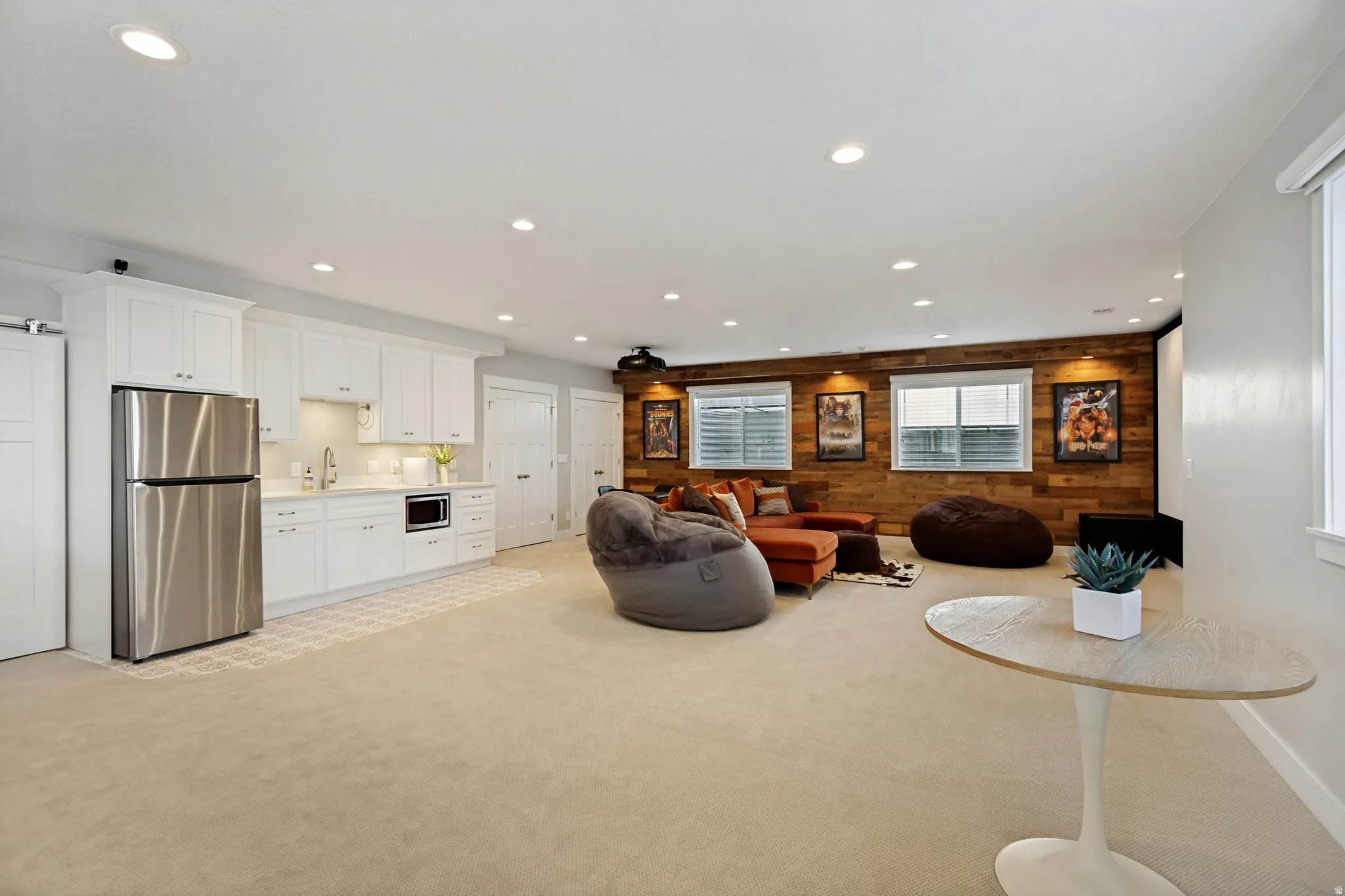 Recessed lighting, wood-finish accent wall, white cabinetry with under-cabinet lighting, stainless steel refrigerator, and built-in microwave