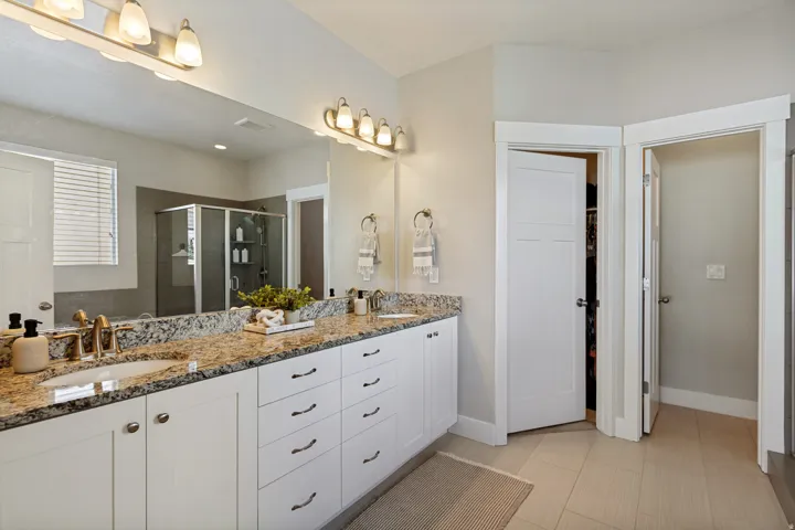 Dual sink vanity with granite countertop, white cabinetry, and brushed nickel fixtures