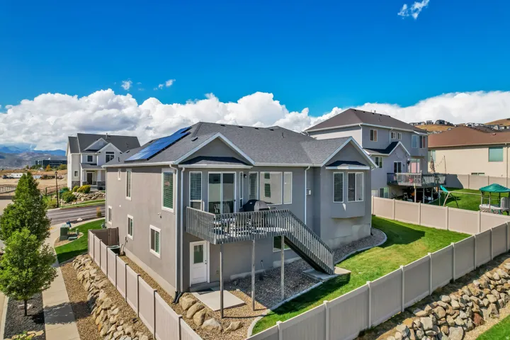 Two-story residence featuring a private deck with exterior stairs, solar panels on the roof, and a fenced backyard with a sloped lawn