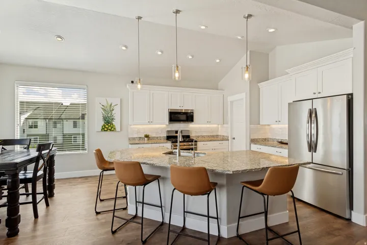 Kitchen featuring a large island with stone countertop, pendant lighting, stainless steel appliances, and white cabinetry