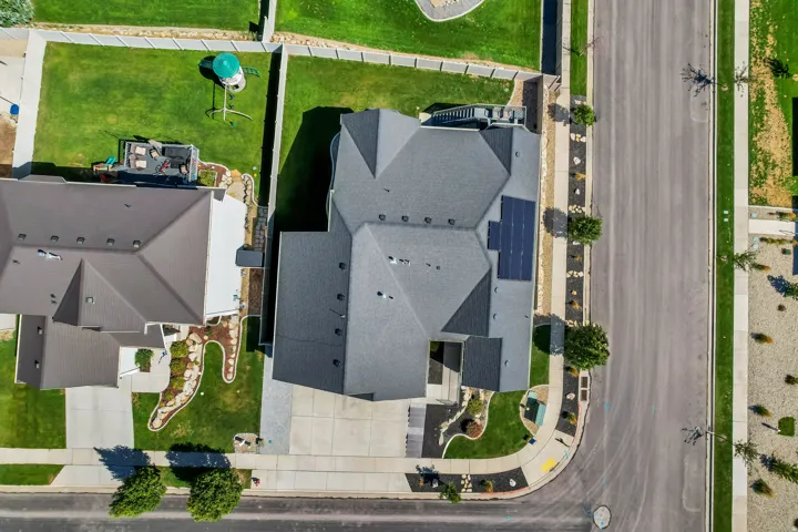 Pitched roofline with solar panels, attached garage, paved driveway, and established landscaping