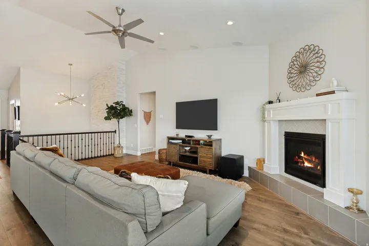 Vaulted ceiling with modern ceiling fan and recessed lighting, wood-finish flooring, white fireplace mantel with tile surround, and open-concept railing