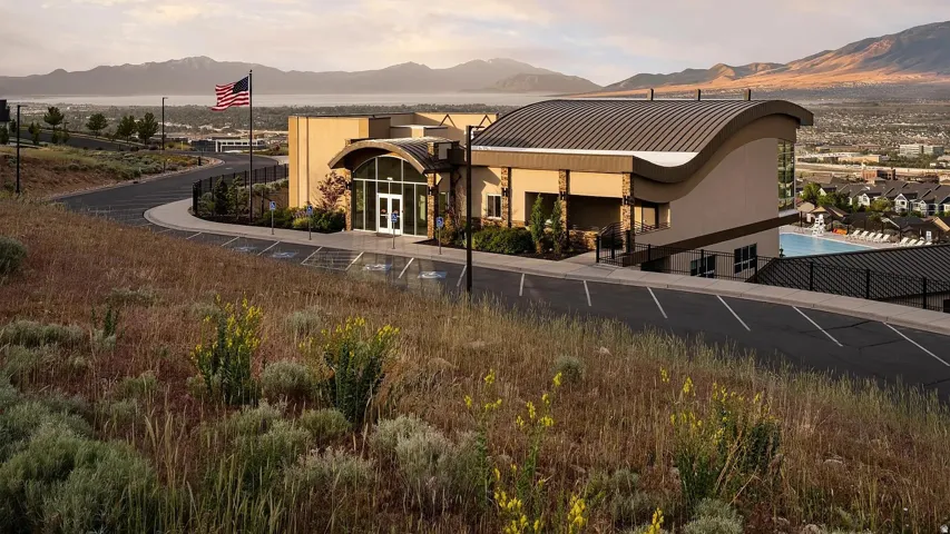 Modern building exterior featuring a curved roofline, expansive glass entrance, and a surrounding paved parking area