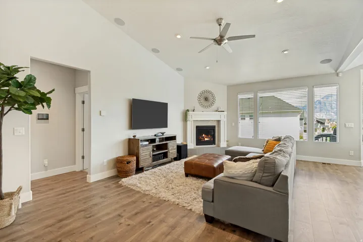 Vaulted ceiling featuring a ceiling fan and recessed lighting, wood-finish flooring, and a fireplace with a white mantel and hearth