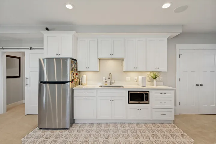 Compact kitchen featuring white shaker cabinetry, stainless steel appliances, a single basin sink, and a patterned tile floor inset