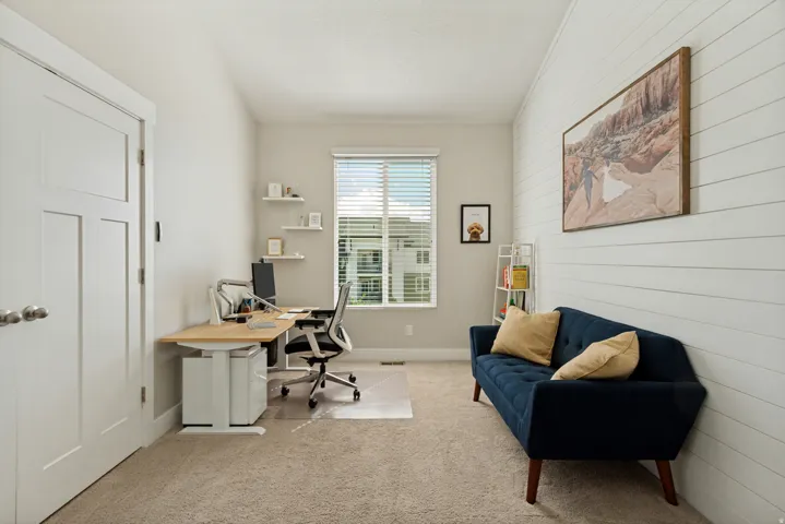 Room featuring a window with blinds, carpeted flooring, a white paneled accent wall, and a solid white door with a three-panel design