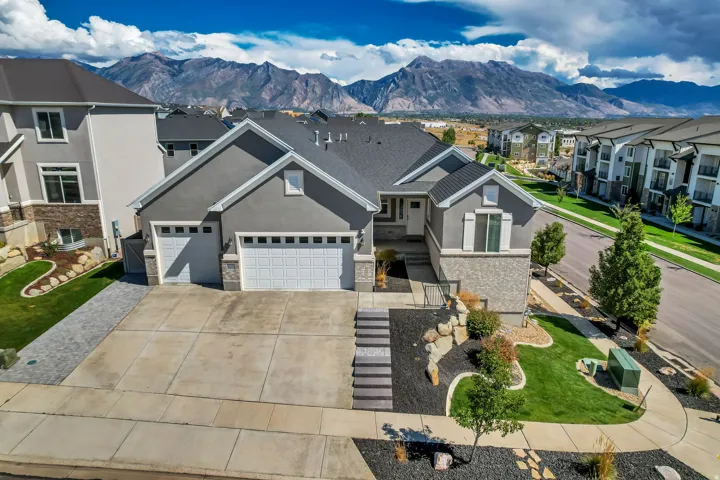 Stucco exterior with stone accents, attached three-car garage, concrete driveway, landscaped front yard, and a stone walkway
