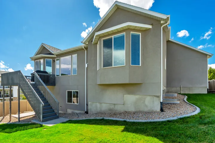 Stucco exterior with multiple windows, a second-story deck with exterior stairs, and a landscaped yard featuring grass and decorative rock