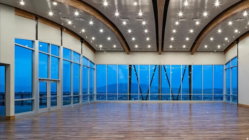 Expansive window walls, wood-finish flooring, vaulted ceilings with exposed wood beams, recessed lighting, and glass-paneled double doors