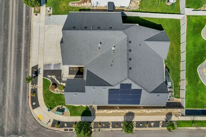 Asphalt shingle roof with solar panel array, concrete driveway, and manicured lawn