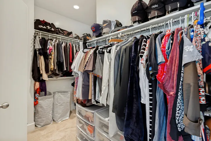 Recessed lighting illuminates the closet featuring multiple hanging rods and integrated shelving