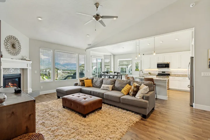 Vaulted ceiling with a ceiling fan, fireplace with a tile surround and mantel, wood-finish flooring, and a kitchen with white cabinetry and stainless steel appliances