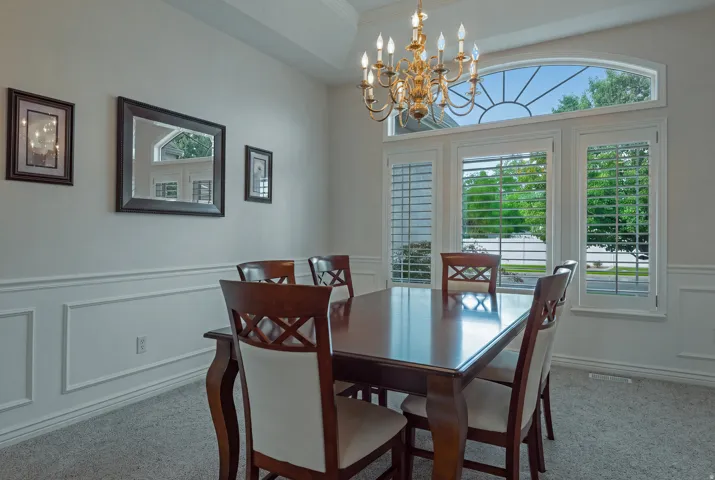 Tray ceiling with a brass chandelier, arched transom window, and plantation shutters