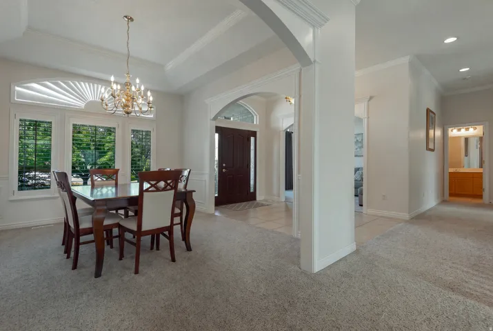 Formal dining area featuring a tray ceiling with a chandelier, plantation shutters, and arched doorways