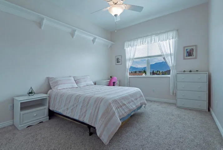 Wall-to-wall carpeting, ceiling fan with integrated lighting, window with mountain backdrop, and crown molding shelf