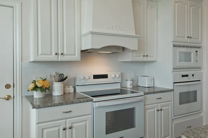 White shaker-style cabinetry, granite countertops, subway tile backsplash, built-in microwave, and wall oven