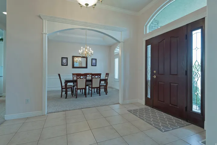Tile flooring, dark wood-finish double entry doors, decorative glass sidelights, arched transom window, and an arched entryway with molding