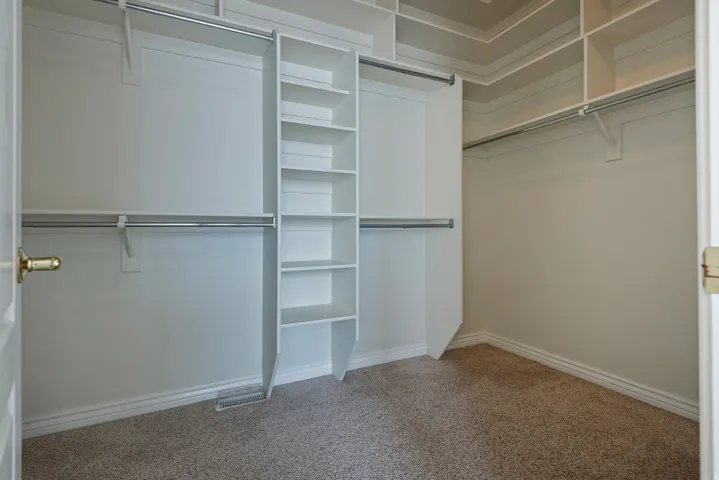 Expansive walk-in closet featuring multiple hanging rods, built-in shelving, and neutral carpeting