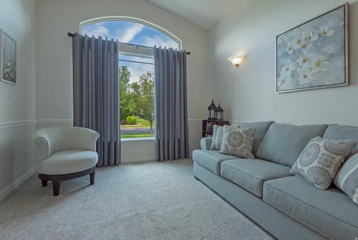 Vaulted ceiling, arched window, wall sconce lighting, wainscoting, and carpeted flooring