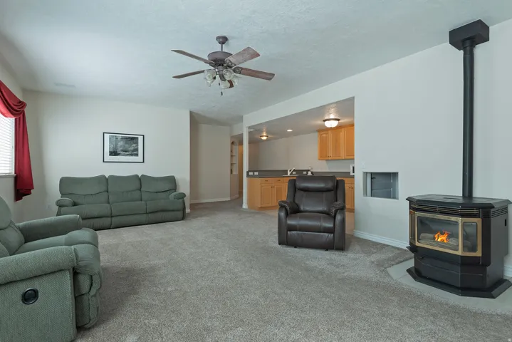 Carpeted living area with a ceiling fan, a built-in stove, and a window with blinds