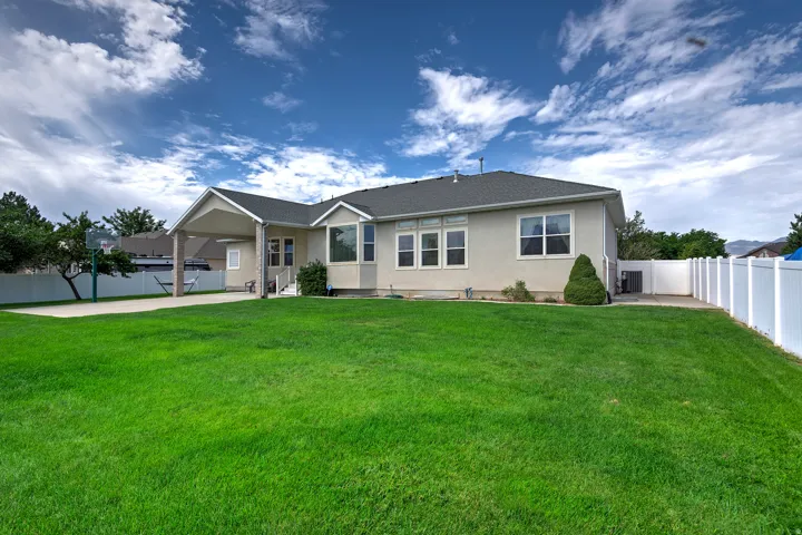 Expansive green lawn, white vinyl fencing, covered patio, concrete patio, and multiple large windows
