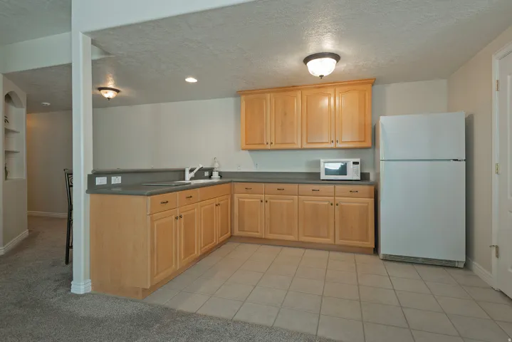 Kitchenette with light wood-finish cabinetry, solid surface countertops, a stainless steel sink, and tile flooring