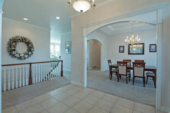 Tiled flooring entrance leading to a carpeted dining area with wainscoting and an arched doorway