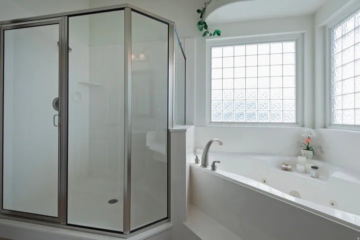 Enclosed glass shower with brushed nickel hardware, built-in bathtub with integrated jets, and privacy block windows