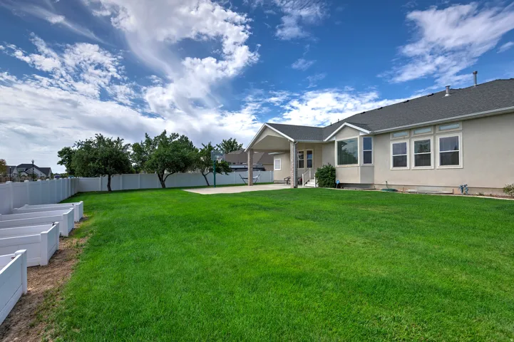 Expansive green lawn, covered patio, privacy fencing, multiple windows, and mature trees